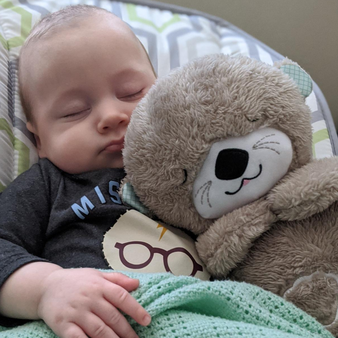 Baby sleeping peacefully with plush bear toy and green blanket, soft bedding in background