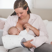 Mother breastfeeding baby with soft pillow in cozy home, baby wearing cloud-print outfit