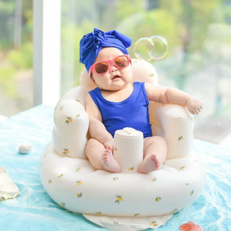 Baby in blue outfit and sunglasses sitting in a cushioned baby chair, educational toy nearby