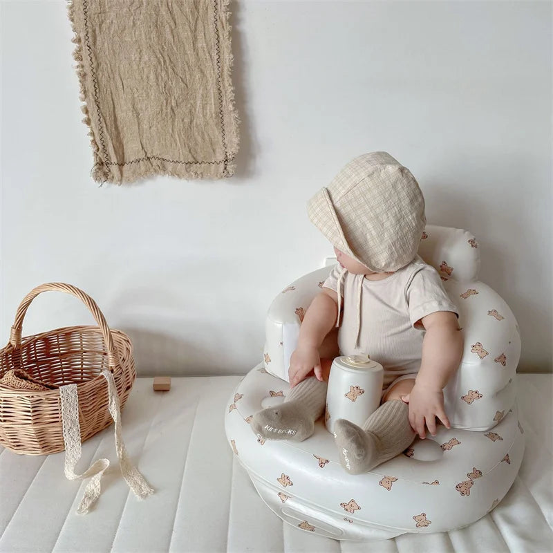 Baby in beige bonnet and romper sitting in bear print baby seat, next to wicker basket