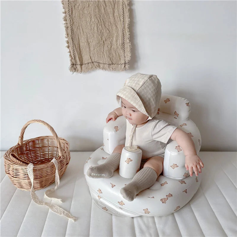 Baby in soft beige outfit and bonnet sitting in bear-print baby seat with wicker basket nearby