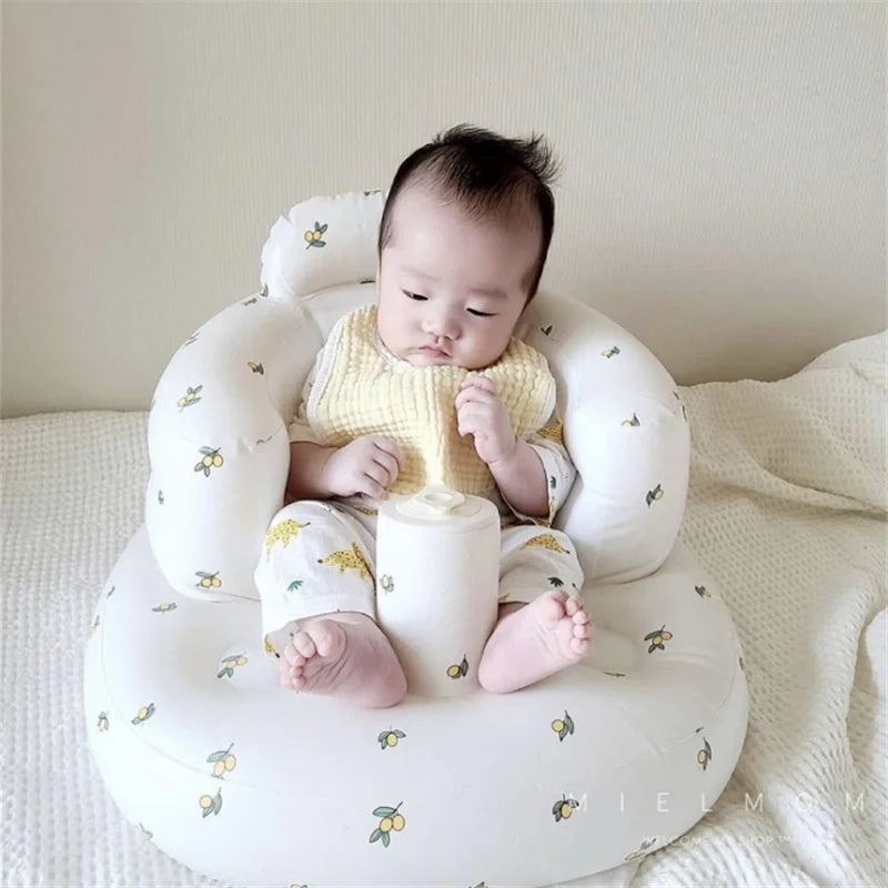 Baby sitting in white floral baby seat, wearing soft bib, on bed, Kid Zone baby essentials