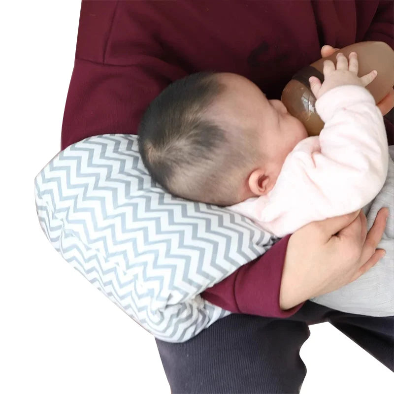 Baby drinking from bottle on gray chevron nursing pillow, parent cradling in arms