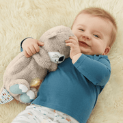 Smiling baby cuddling a plush otter calming toy on a soft cream rug, baby essentials